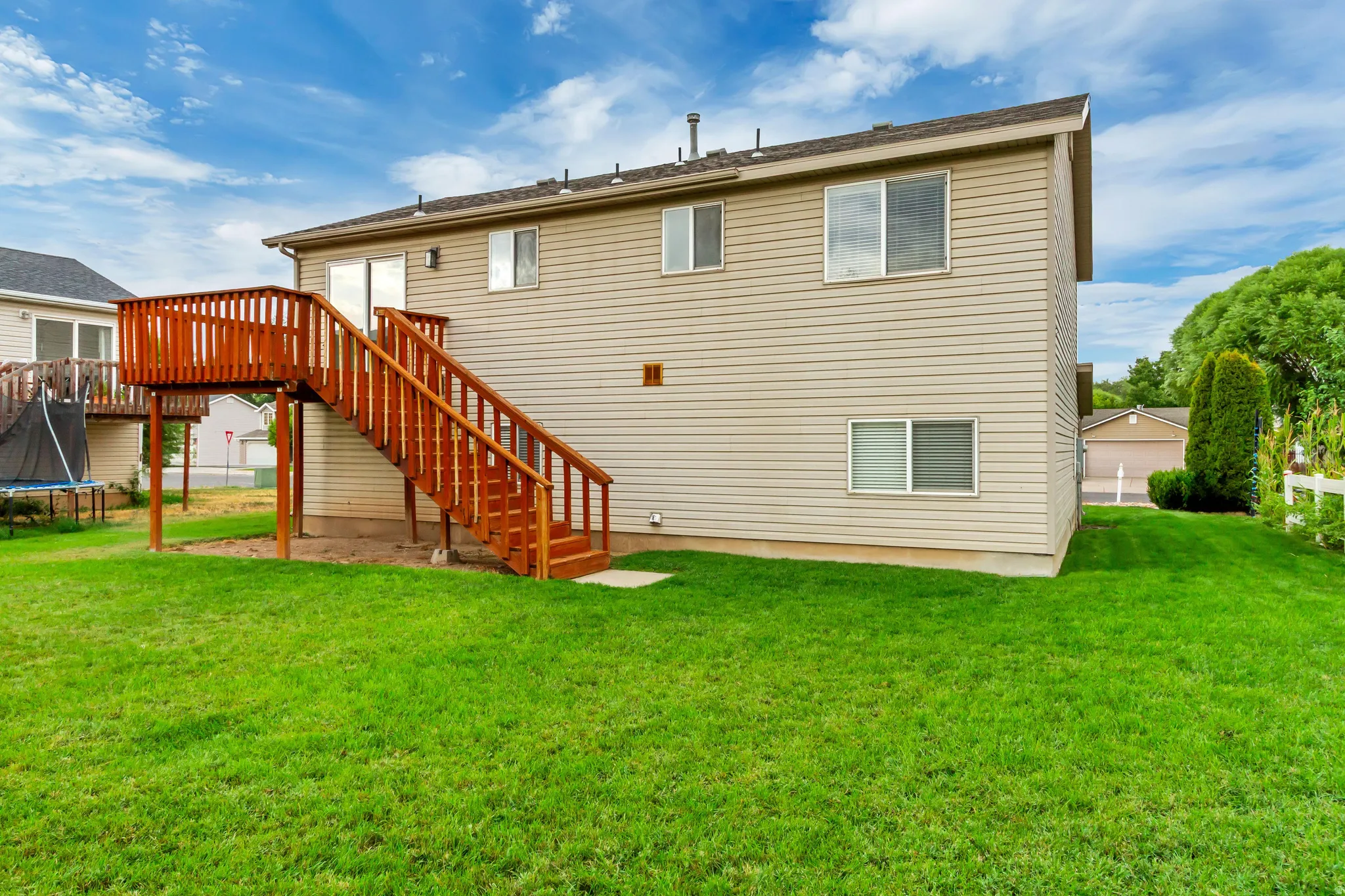 Rear exterior featuring siding, upper-level deck with wood railing and stairs, sliding glass door, and a grassy yard
