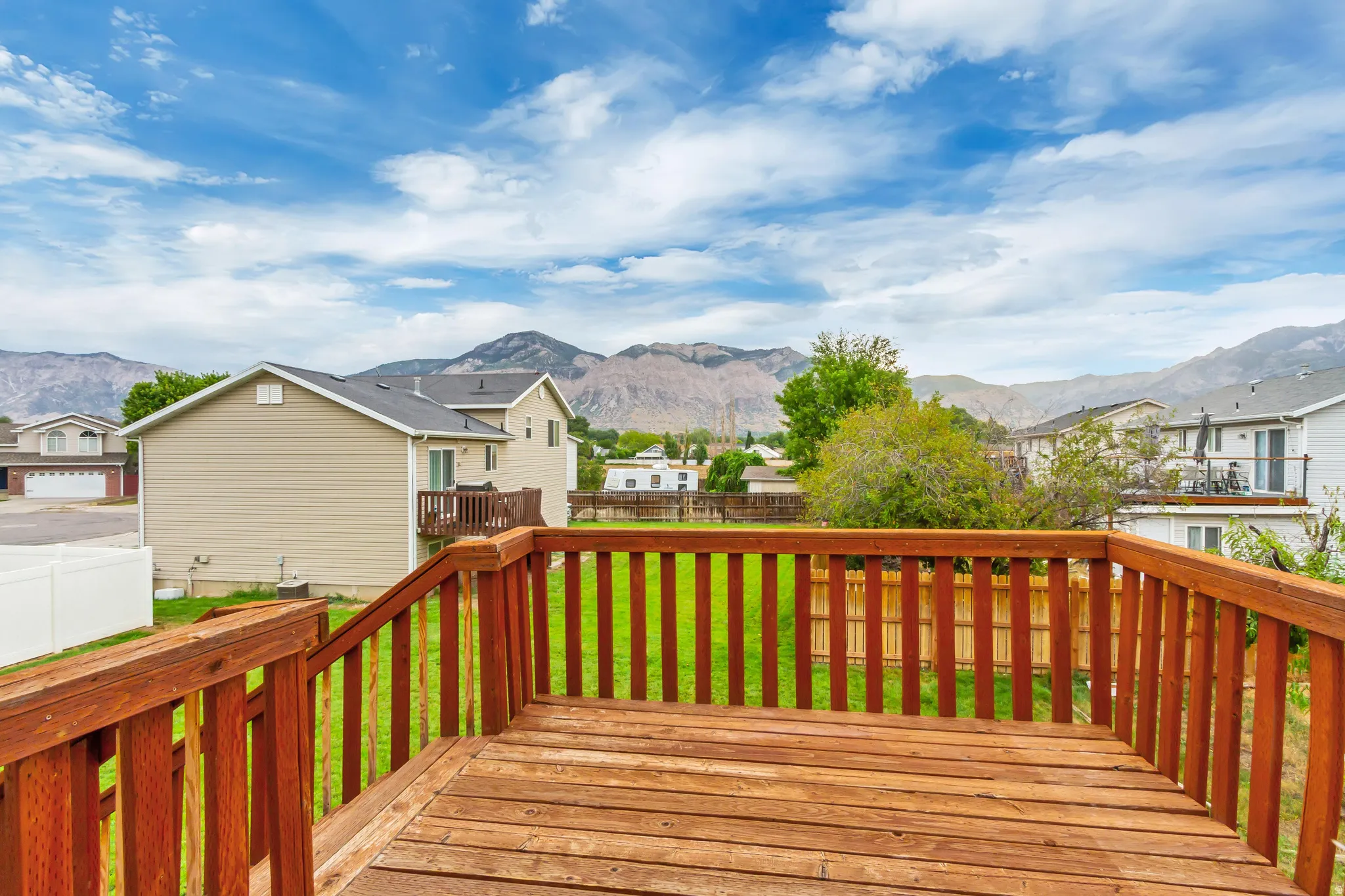 Spacious wood deck with railing overlooking a fenced yard and mountain backdrop