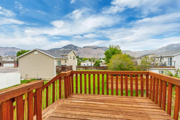 Spacious wood deck with railing overlooking a fenced yard and mountain backdrop