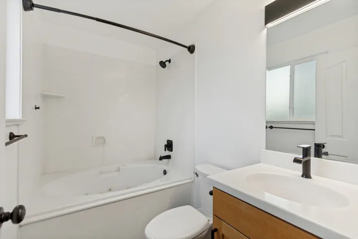 Bathroom featuring a jetted tub, a vanity with a light wood-finish cabinet, a white countertop with an integrated sink, and matte black fixtures