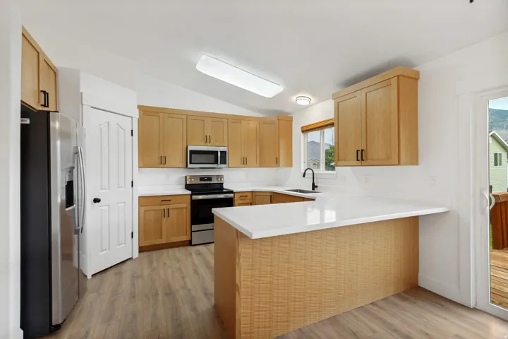 Kitchen featuring wood-finish cabinetry, stainless steel appliances, white countertops, and wood-finish flooring