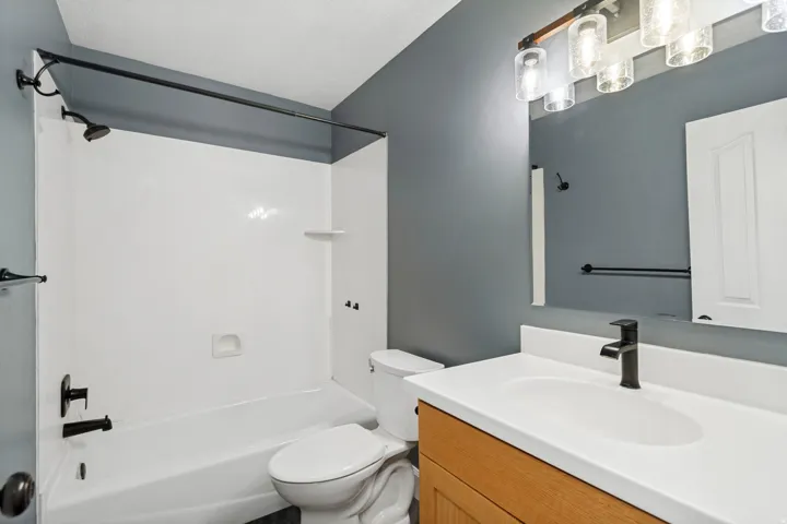 Bathroom featuring a bathtub with an integrated shower, matte black fixtures, wood-finish vanity with an integrated sink, white countertop, and a wall-mounted medicine cabinet