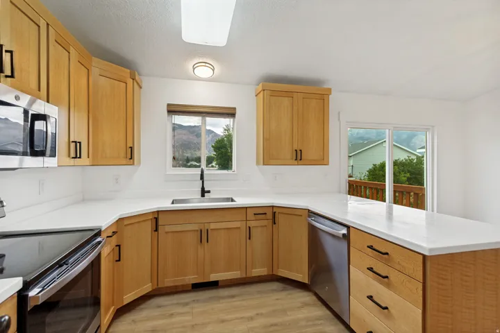 Kitchen featuring wood-finish cabinetry, stainless steel appliances, white countertops, and wood-finish flooring