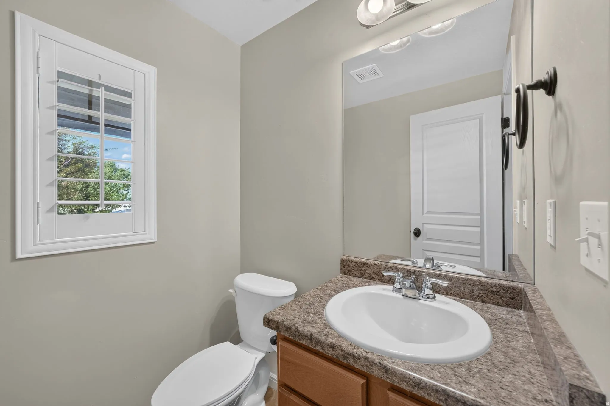 White plantation shutters, wood-finish vanity, speckled countertop, undermount sink, and wall-mounted mirror