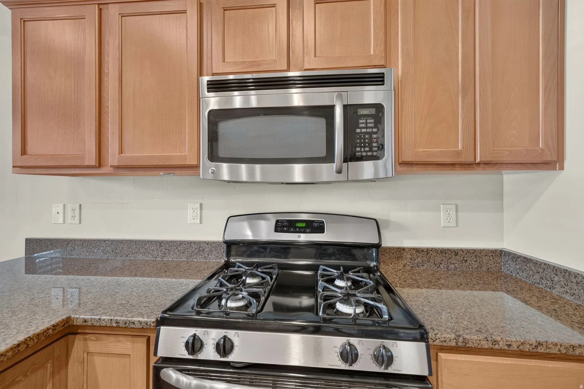 Stainless steel range, stainless steel microwave, light wood-finish cabinetry, and stone-finish countertops
