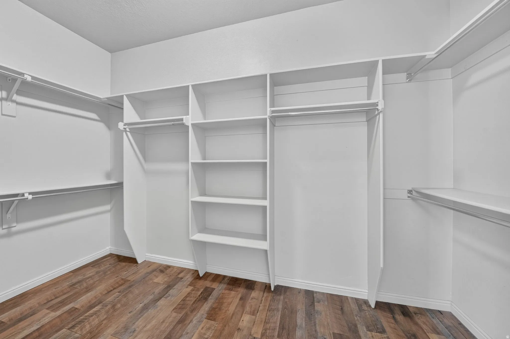 Walk-in closet featuring built-in shelving, multiple hanging rods, and wood-finish flooring