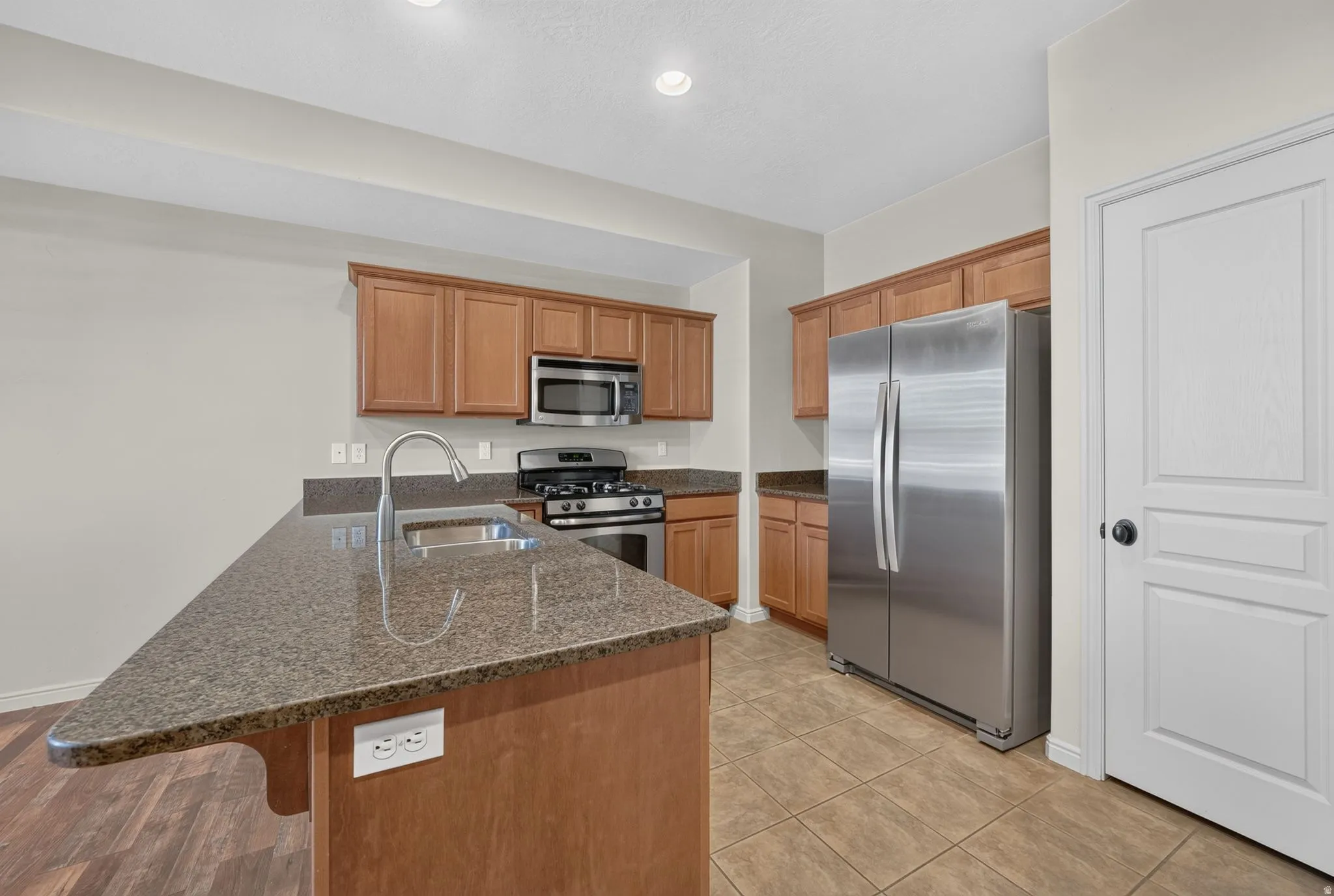 Kitchen featuring a center island with sink, wood-finish cabinetry, stainless steel appliances, and tile flooring