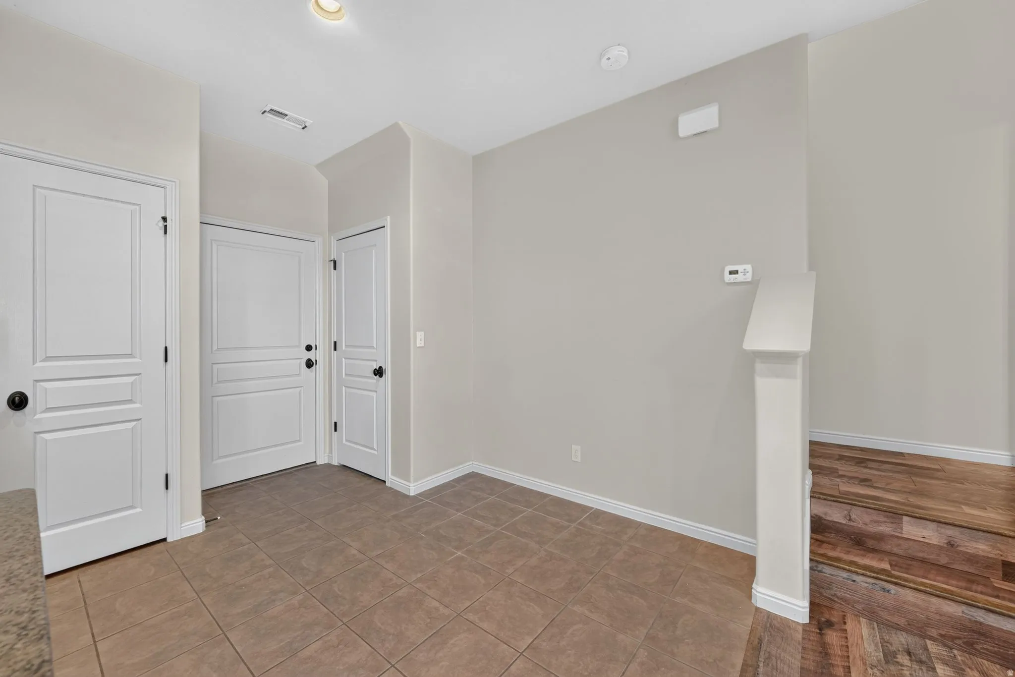 Tile flooring, white paneled doors with matte black hardware, neutral wall tones, and wood-finish stair treads