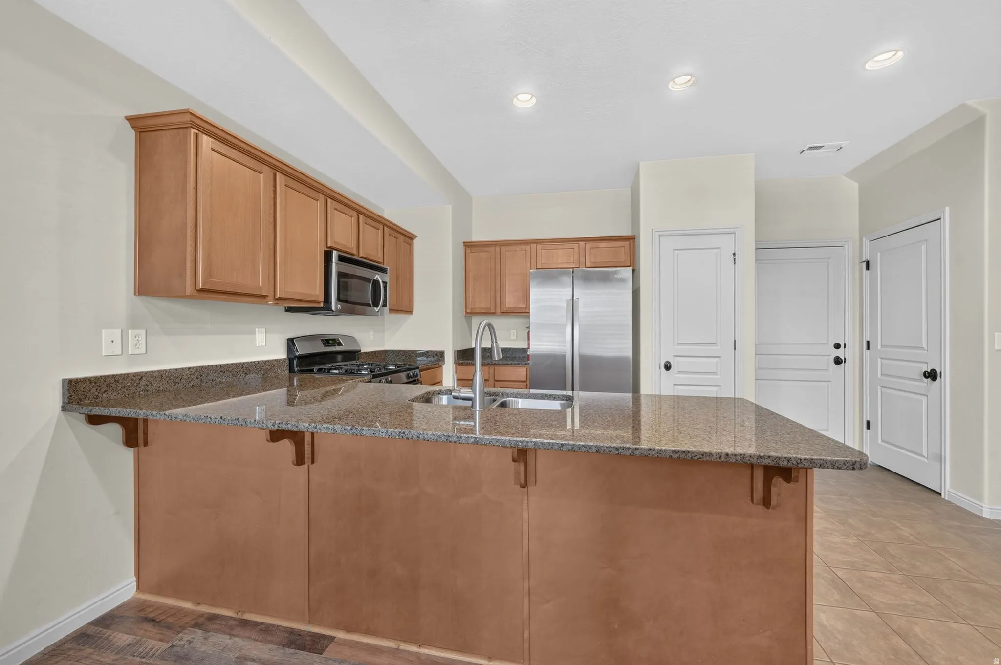 Kitchen featuring wood cabinetry, stainless steel appliances, a large island with an undermount sink, and recessed lighting