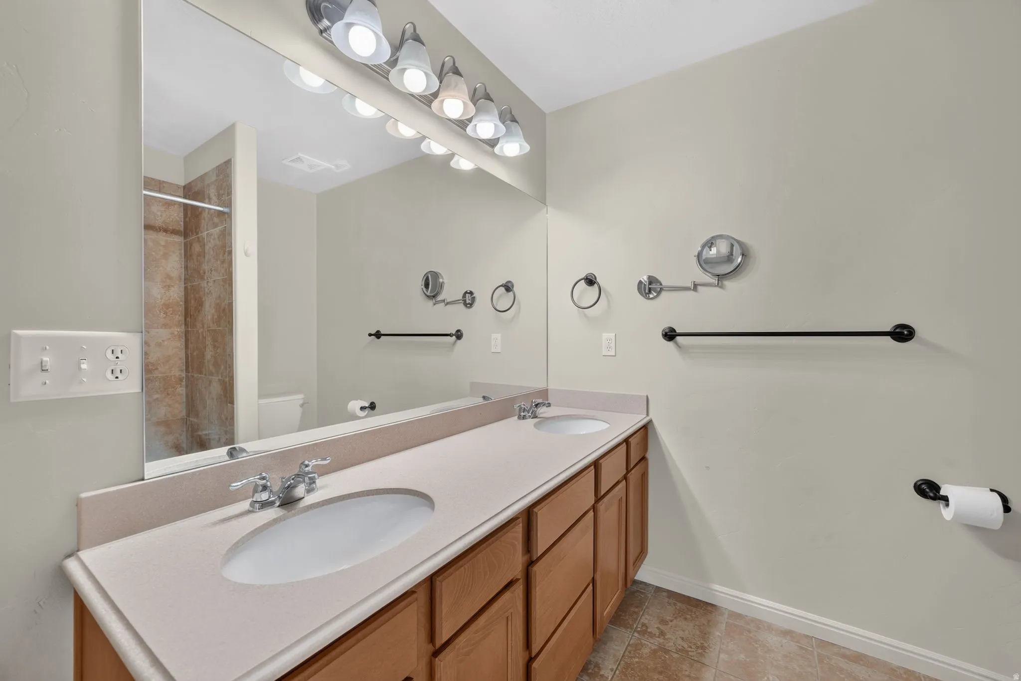 Dual undermount sinks with chrome fixtures, integrated countertop, wood-finish cabinetry, and a full-width vanity mirror
