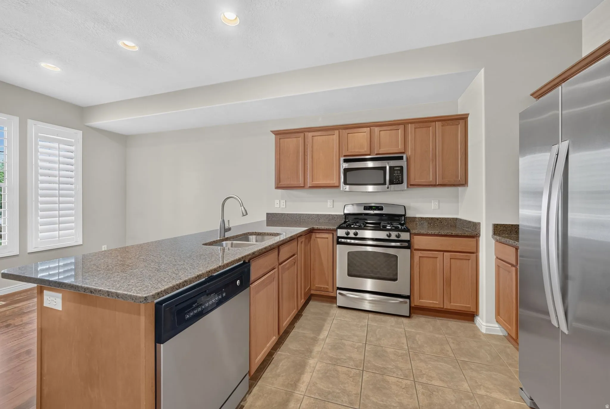 Kitchen featuring wood cabinetry, stainless steel appliances, granite-style countertops, an integrated kitchen island with a double basin sink, and tile flooring