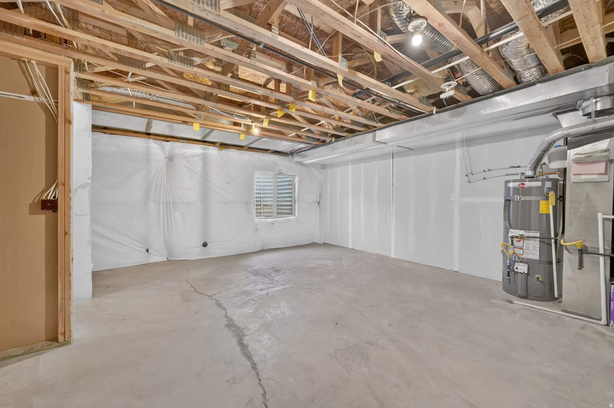 Unfinished basement space with exposed ceiling joists, concrete flooring, and an installed water heater