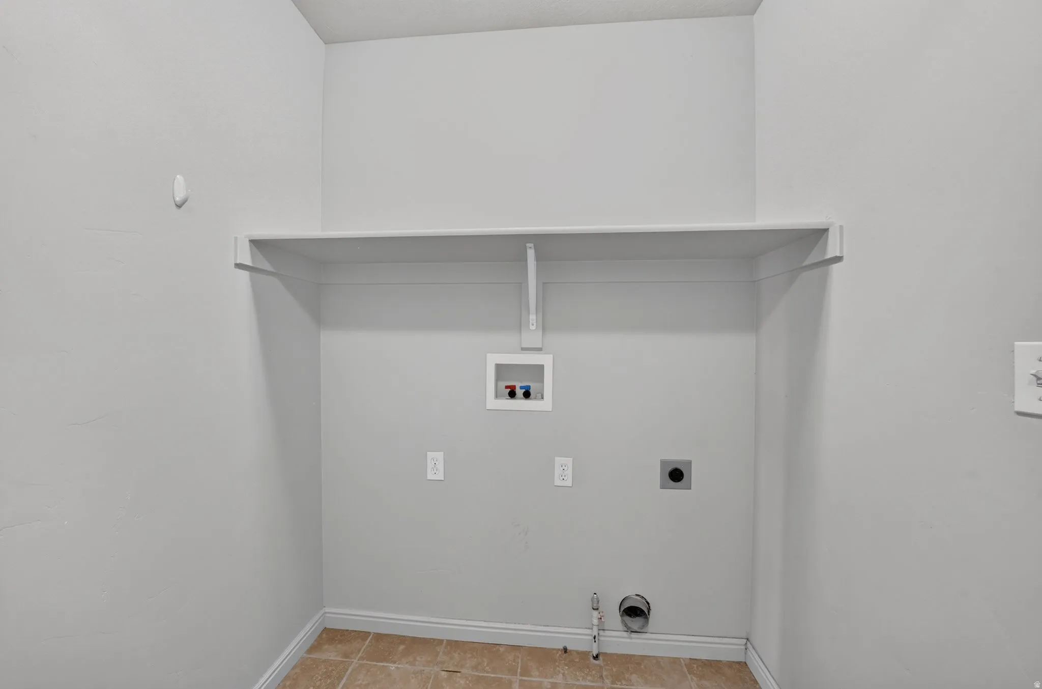 Dedicated utility space featuring a built-in shelf, plumbing hookups, electrical outlets, and tile flooring