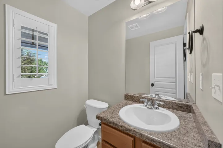 White plantation shutters, wood-finish vanity, speckled countertop, undermount sink, and wall-mounted mirror