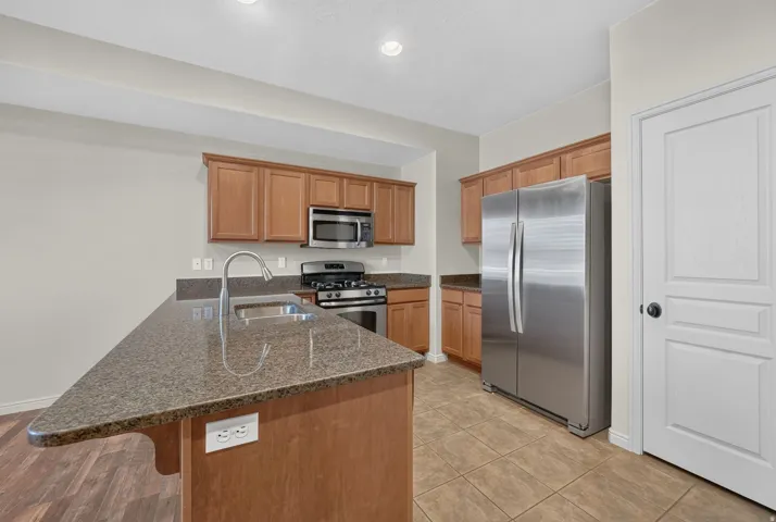 Kitchen featuring a center island with sink, wood-finish cabinetry, stainless steel appliances, and tile flooring