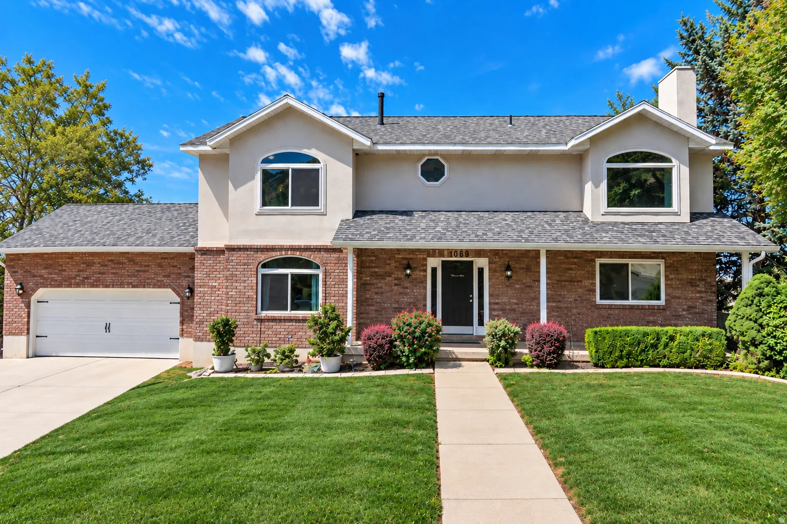 Brick and stucco exterior, two-car garage, multiple arched windows, prominent front entry, and established landscaping