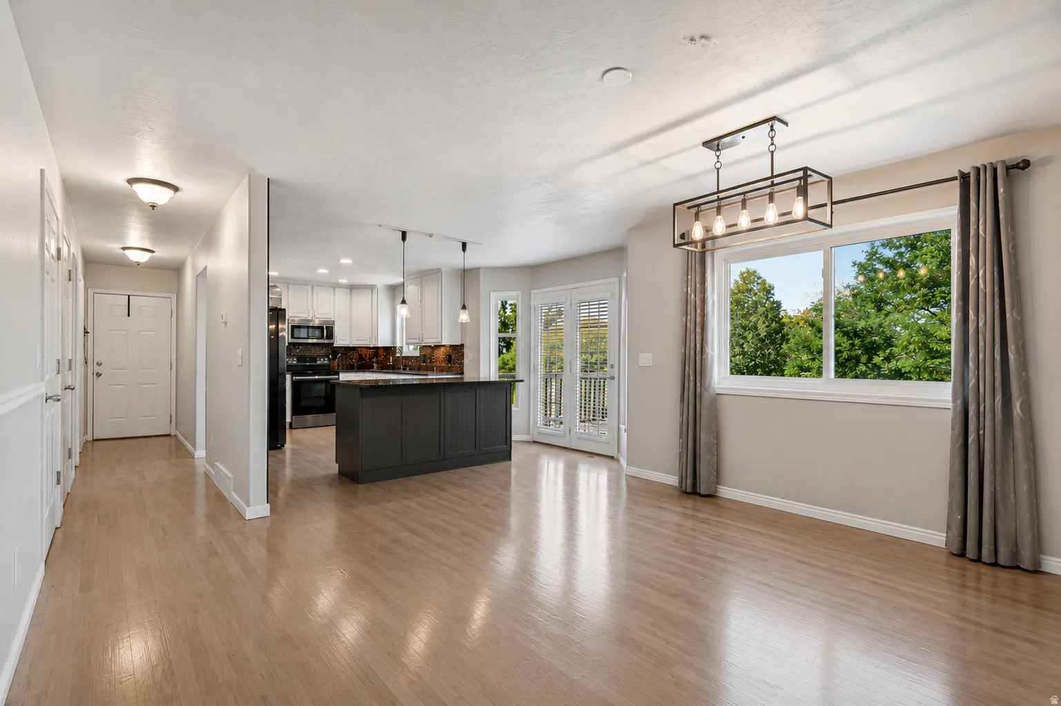 Open kitchen and dining area, French doors to large valley-view deck, kitchen island, abundant cabinets and counter space, large windows, custom decorative wall, and plenty of natural light