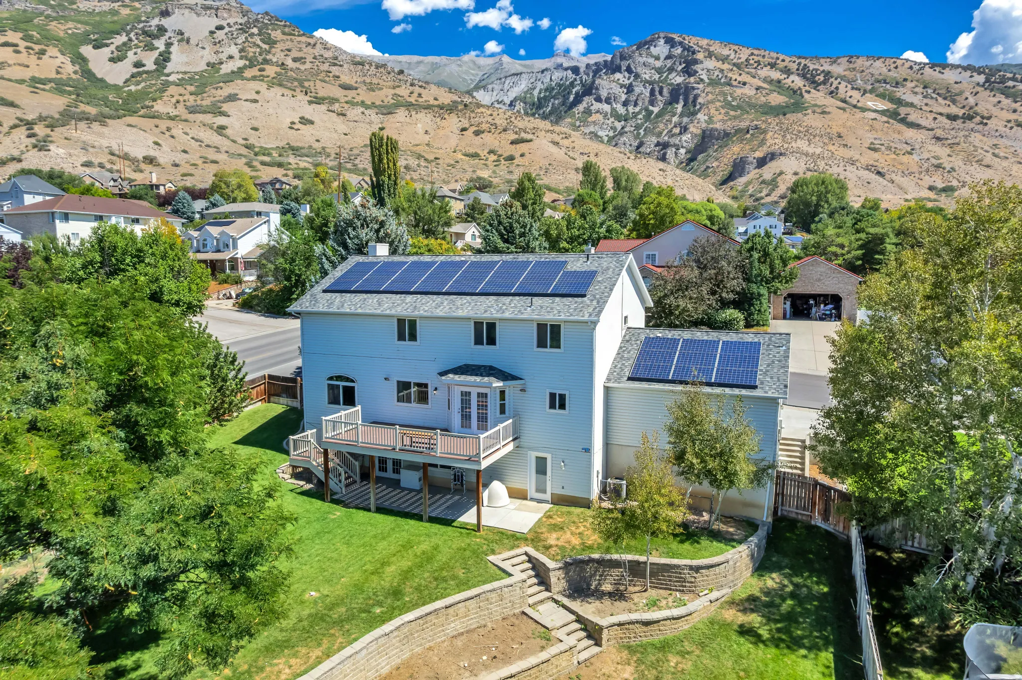 Rear exterior featuring a two-story deck, ground-level patio, and terraced landscaping
