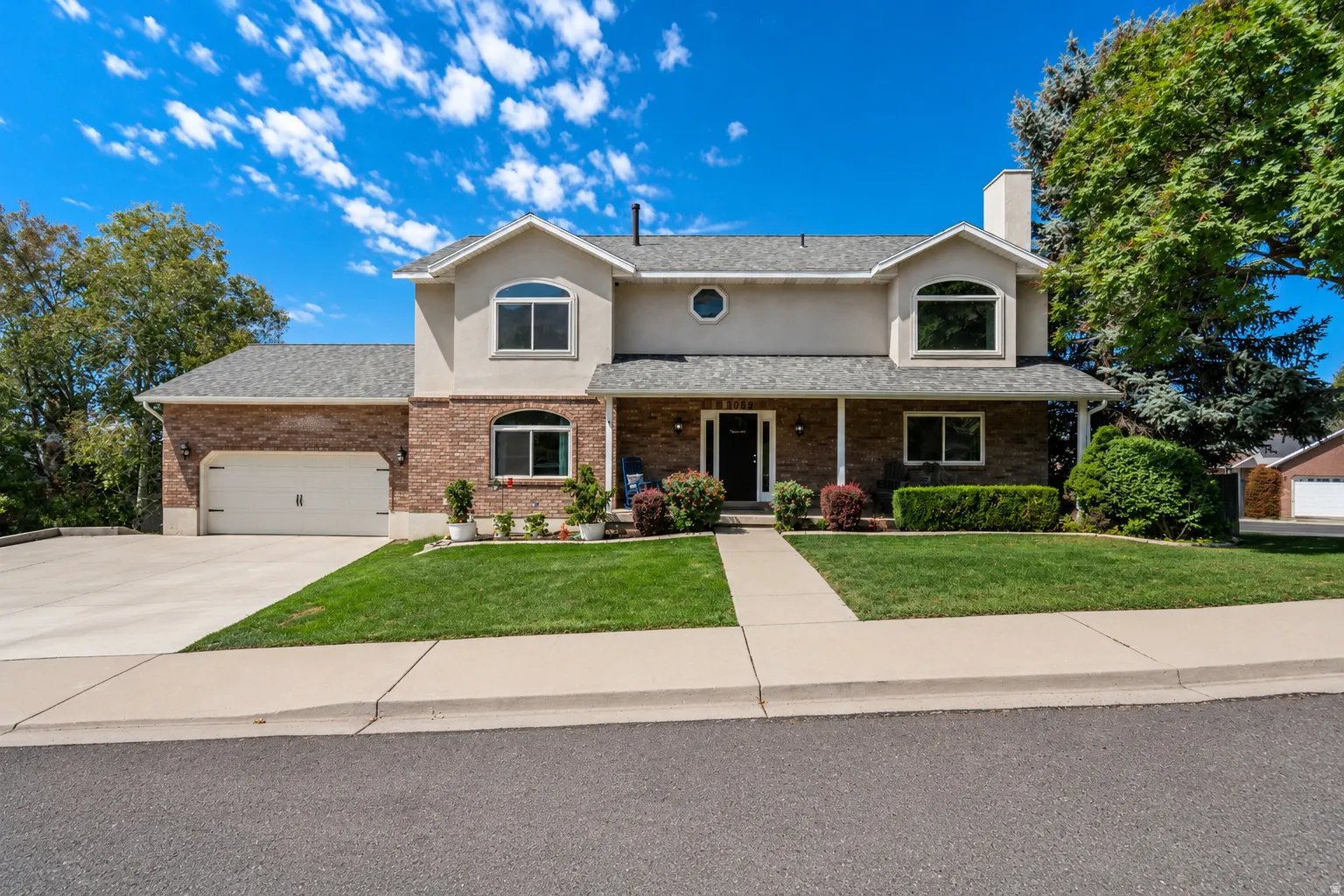 Inviting brick and stucco exterior with a 2 car attached garage, covered front porch, arched windows, and oversize  concrete driveway