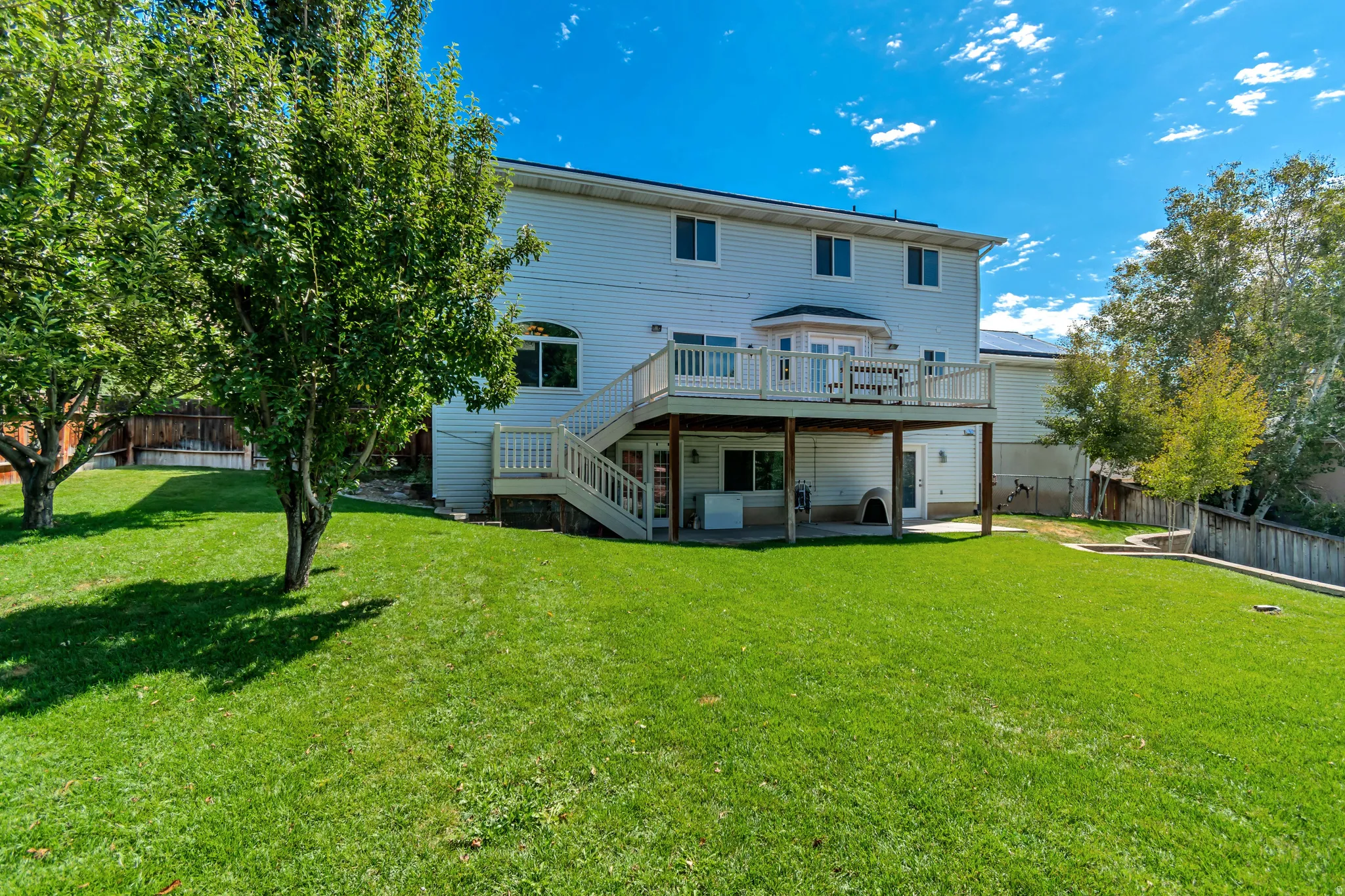 Expansive backyard featuring a manicured lawn, mature trees, and a multi-level deck with white railings