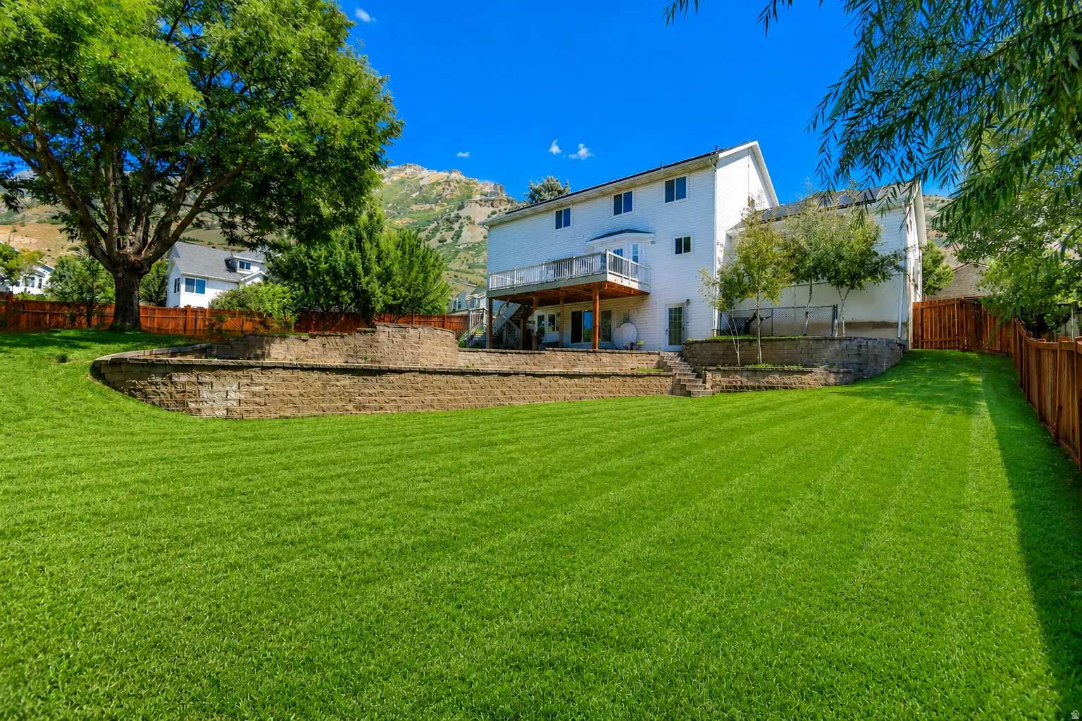 Expansive backyard with a manicured lawn, tiered retaining walls, and a wooden privacy fence