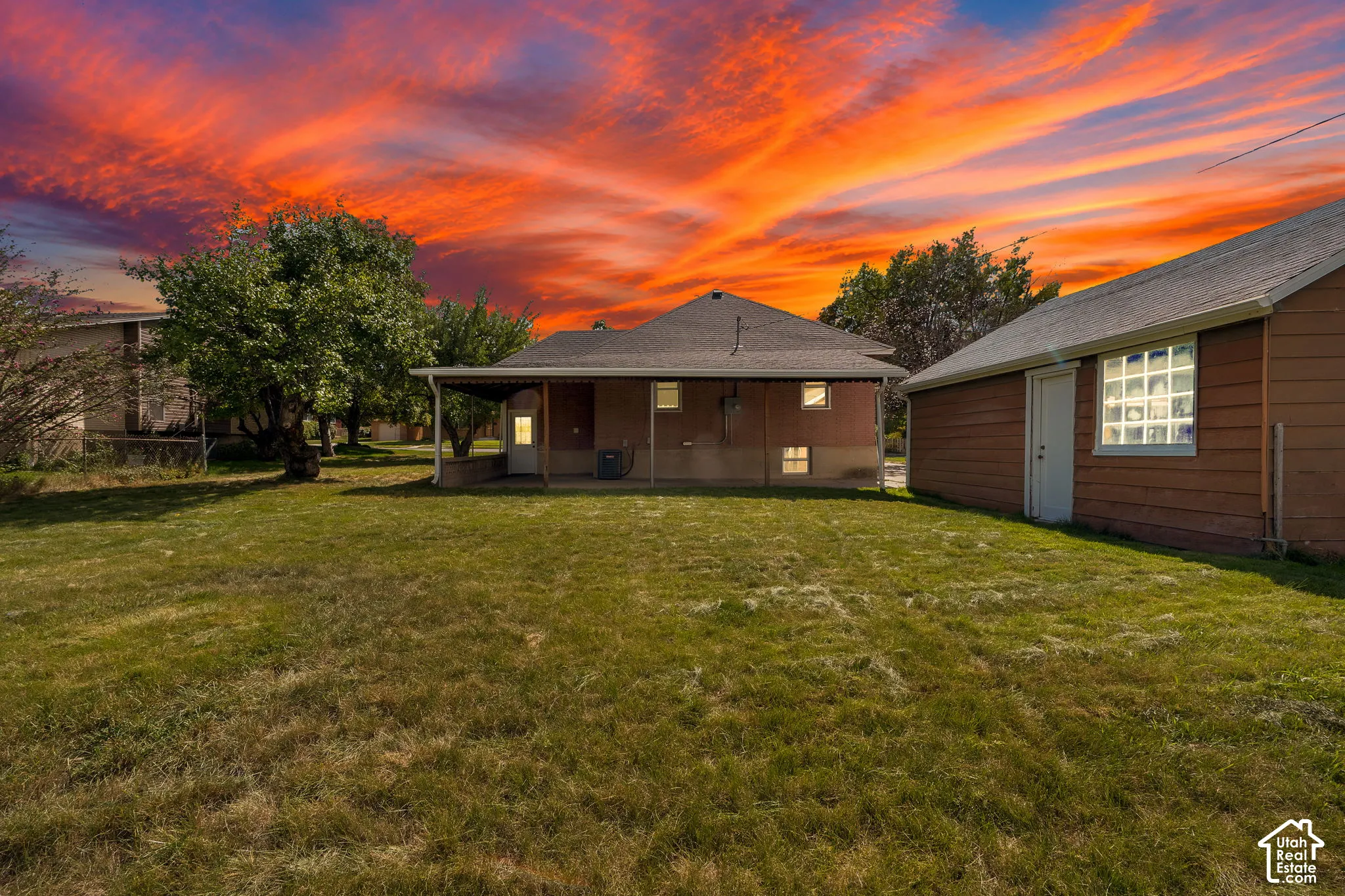 Expansive lawn area, mature trees, single-story residence, covered patio, and detached outbuilding with glass block window