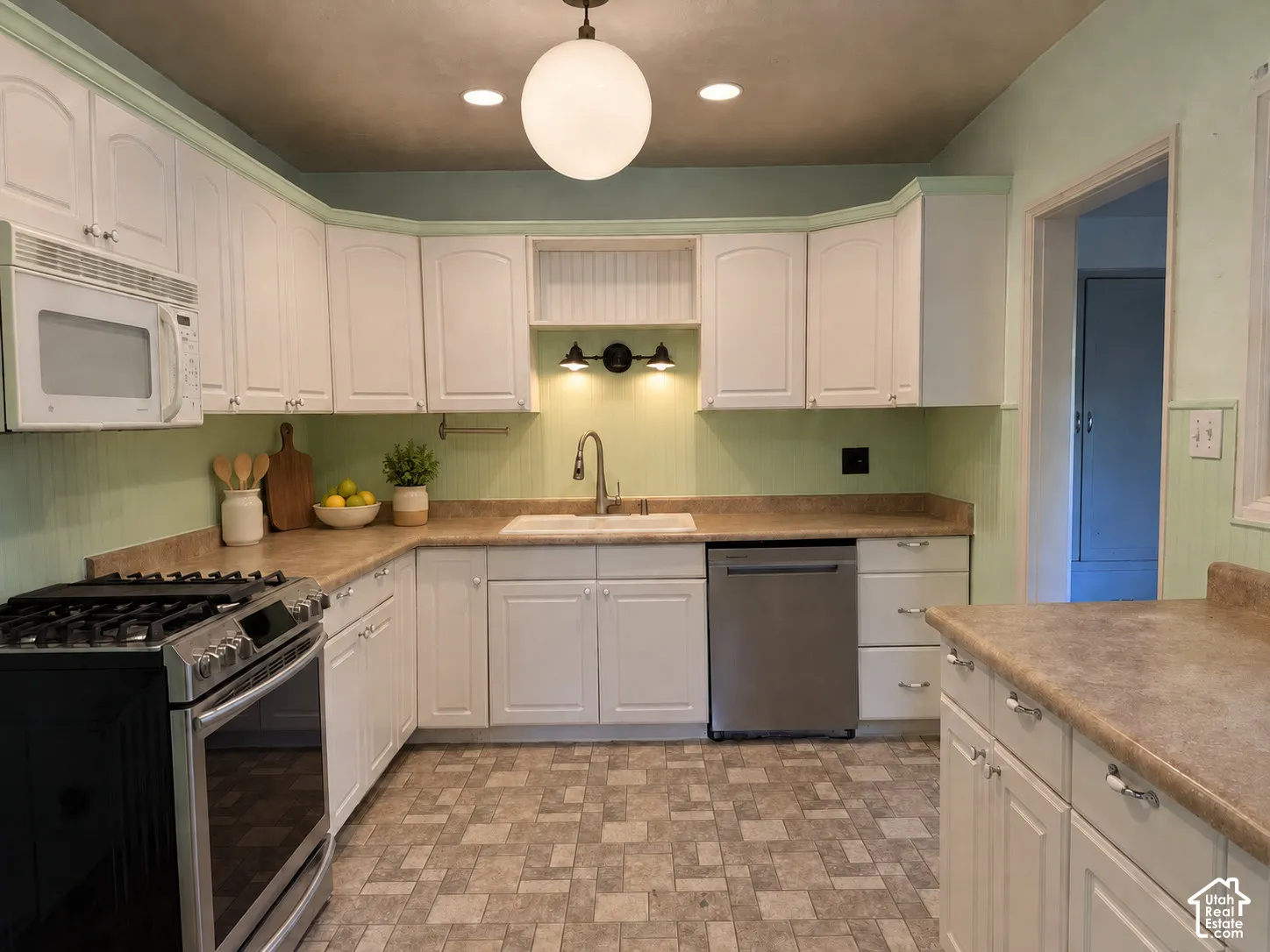White cabinetry with metal hardware, light-toned countertops, stainless steel appliances, and patterned flooring