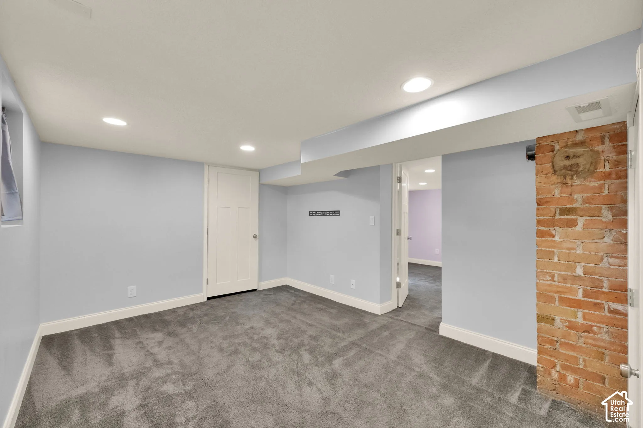 Carpeted room with recessed lighting, exposed brick column, and white trim