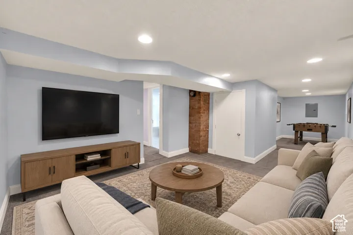 Recessed lighting throughout, exposed brick accent, light blue wall paint, and gray carpet flooring