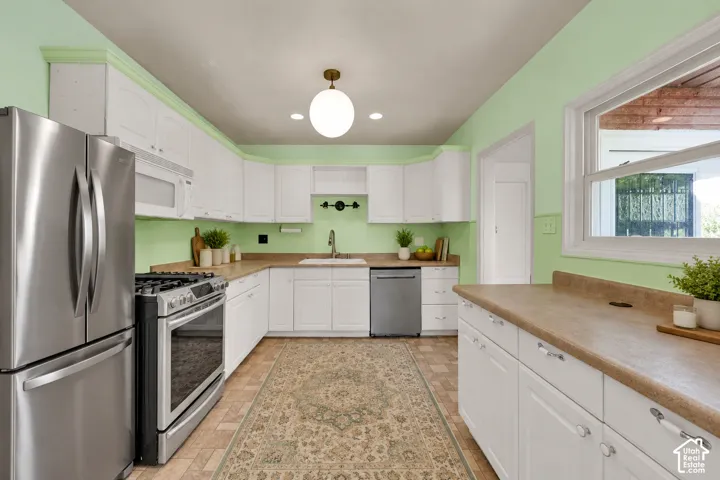White cabinetry with brass hardware, stainless steel appliances, and a window above the sink