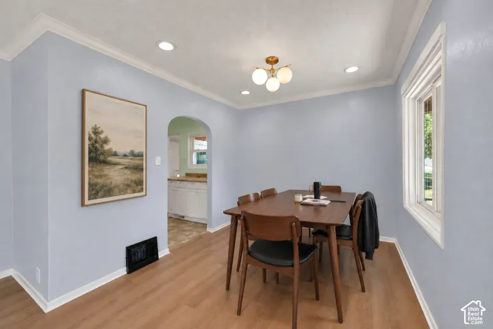 Wood-finish flooring, recessed lighting, crown molding, arched doorway, and a modern ceiling fixture