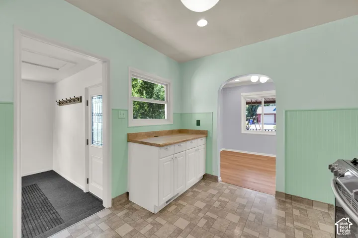Arched doorway opening, wood-finish flooring, built-in lower cabinetry, window with natural light, and patterned floor tile
