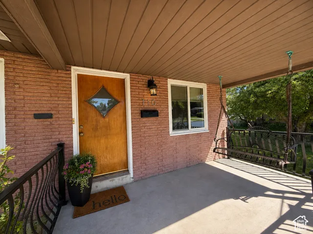 Covered front porch featuring a wood-finish entry door with decorative glass, brick exterior, and a black wrought iron railing