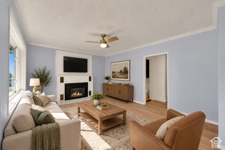 Gas fireplace with a white mantel, wood-finish flooring, ceiling fan, and crown molding