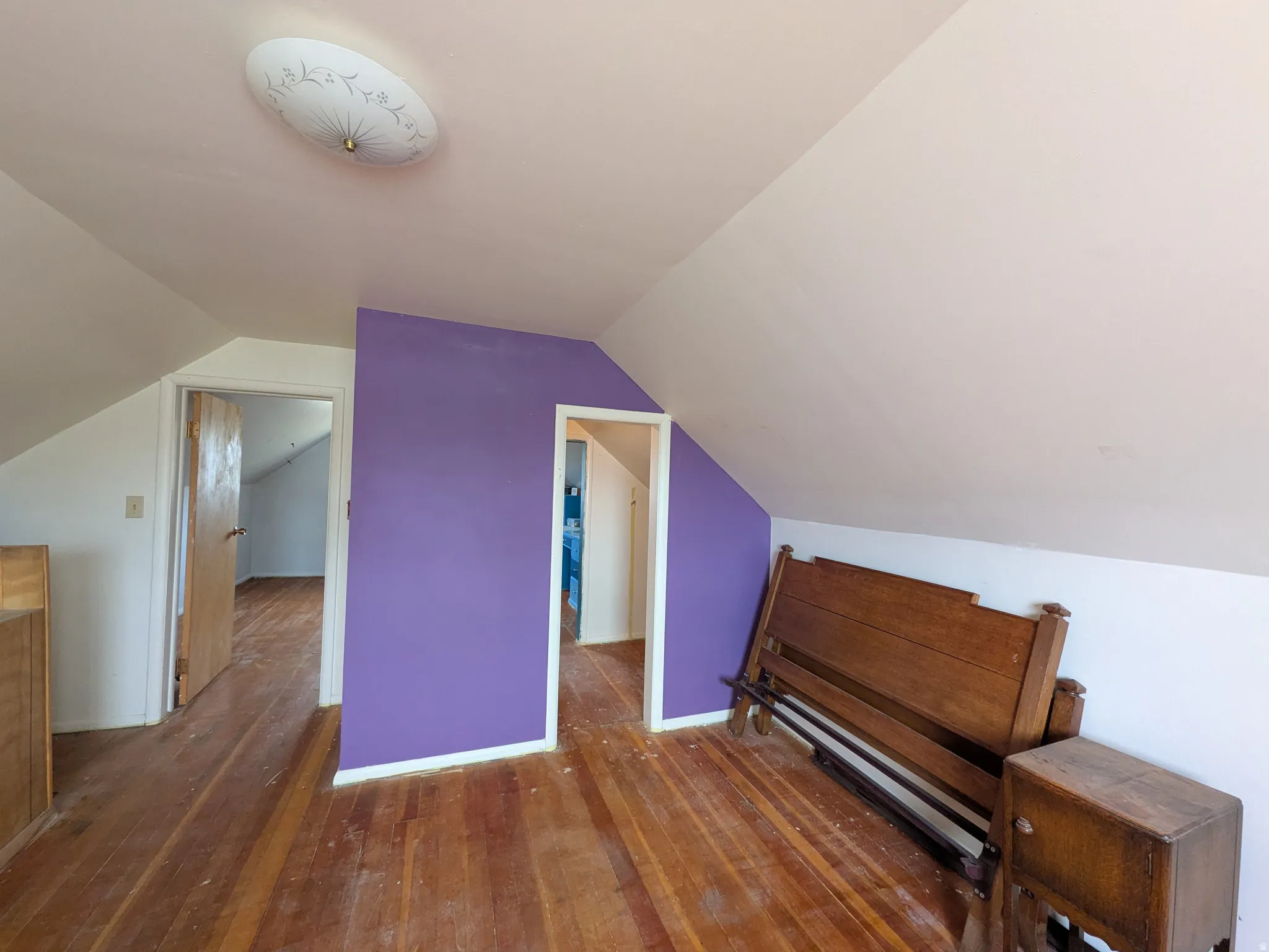 Wood-finish flooring throughout, sloped ceilings, white wall finishes, and a flush-mount ceiling light fixture