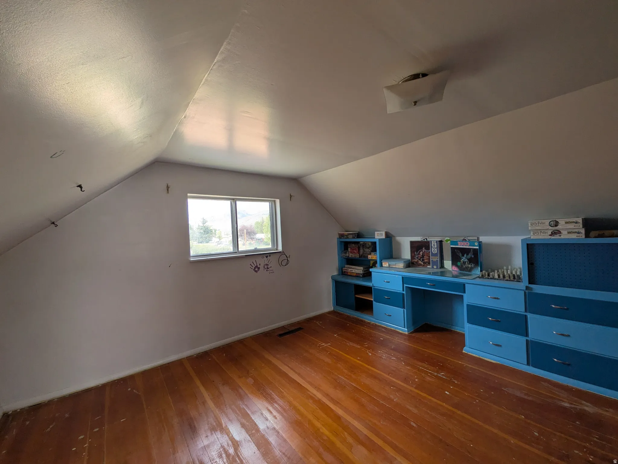 Wood-finish flooring, built-in cabinetry with desk, single window, sloped ceilings, and ceiling-mounted light fixture