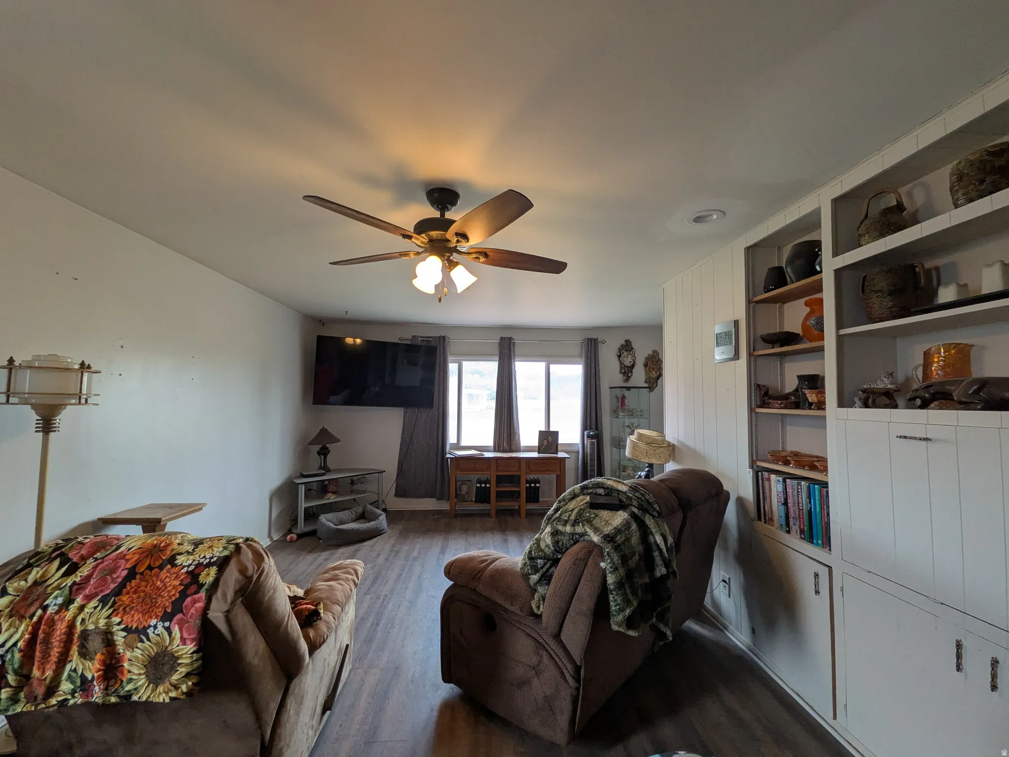 Open-concept living area with wood-finish flooring, a ceiling fan with integrated lighting, and a built-in shelving unit with cabinet storage