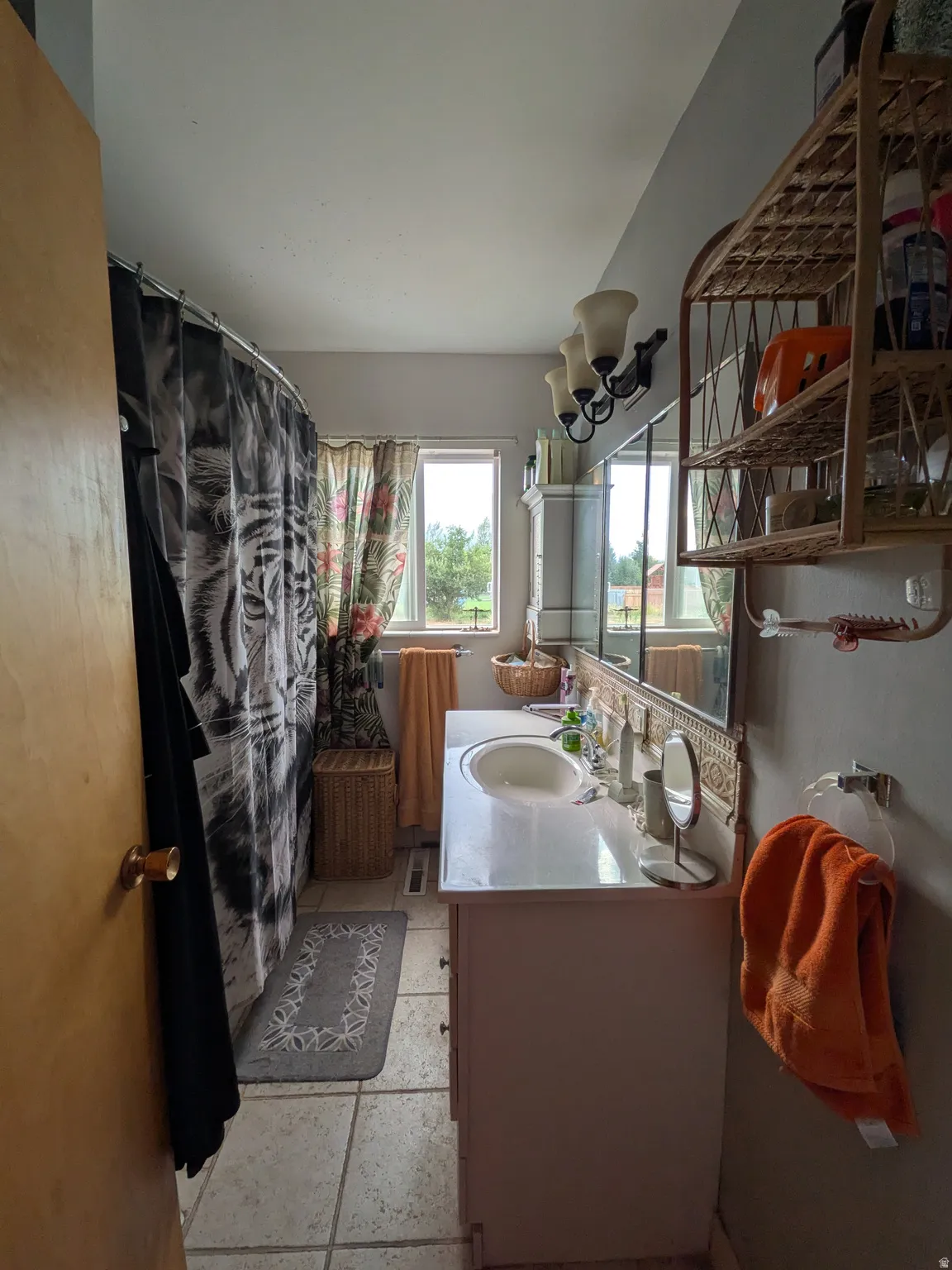 Bathroom featuring a single vanity with an integrated sink, wall-mounted light fixture, tile flooring, and a window
