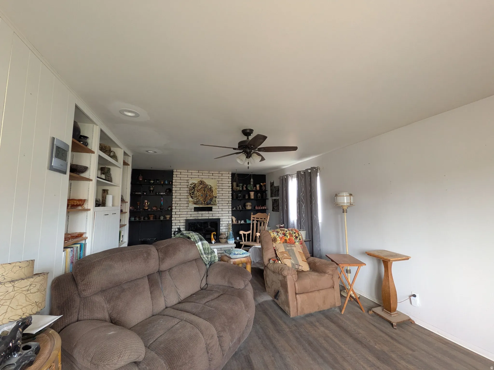 Wood-finish flooring, recessed lighting, ceiling fan, built-in shelving, and a brick fireplace