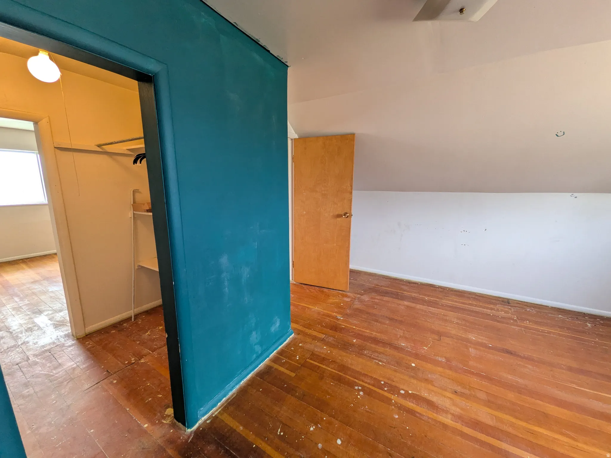 Wood-finish flooring throughout, sloped ceiling, and a built-in closet with shelving