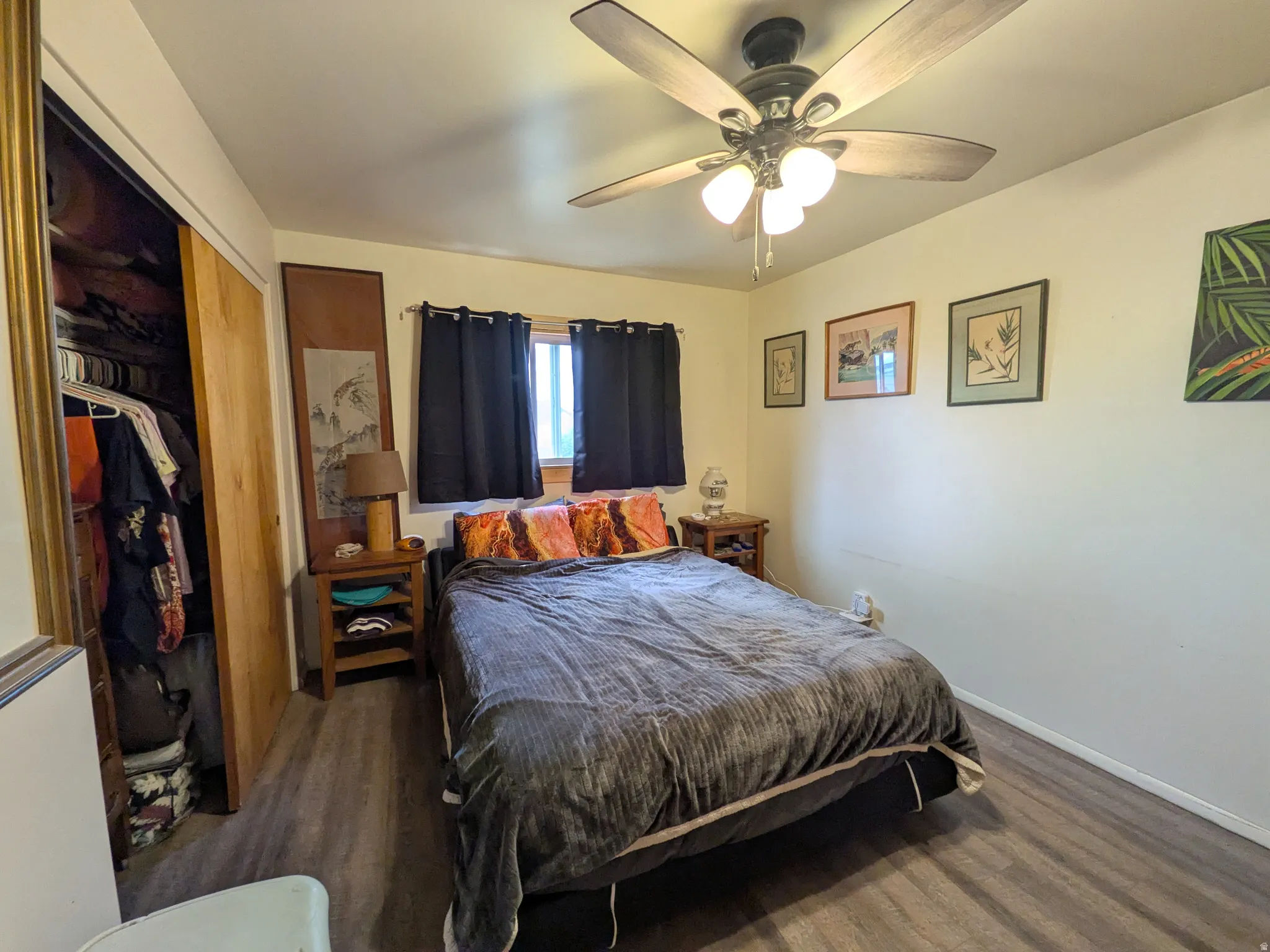 Wood-finish flooring, ceiling fan with integrated lighting, window with dark drapes, and a built-in closet with solid wood doors