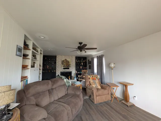 Wood-finish flooring, recessed lighting, ceiling fan, built-in shelving, and a brick fireplace