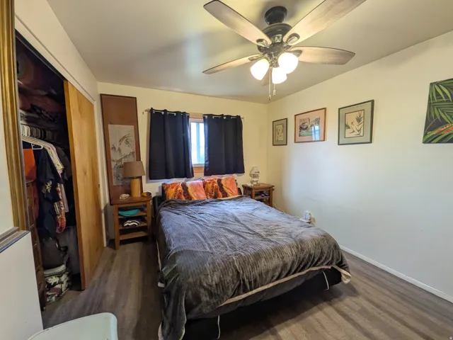 Wood-finish flooring, ceiling fan with integrated lighting, window with dark drapes, and a built-in closet with solid wood doors