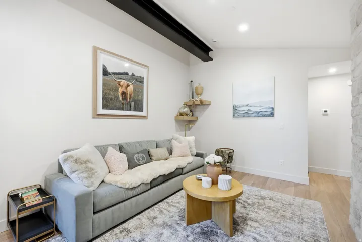 Exposed ceiling beam, light wood-finish flooring, recessed lighting, floating wall shelves, and a textured stone wall