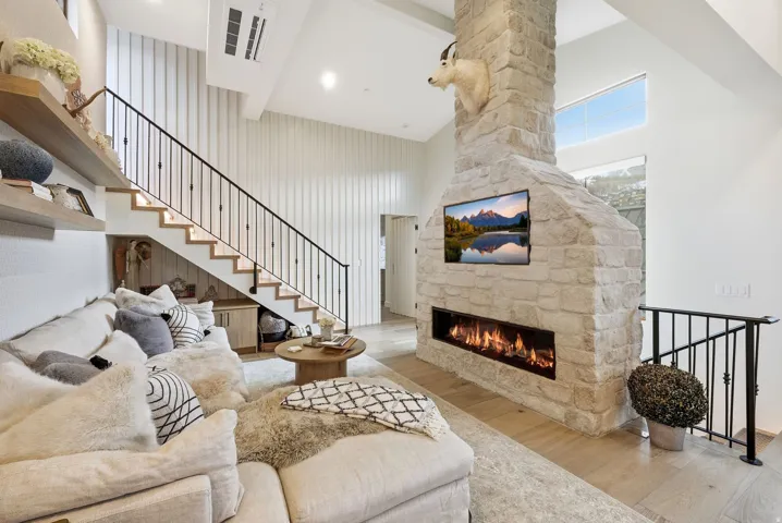 Stone fireplace with a linear firebox, wood-finish flooring, staircase with a wrought iron railing, vaulted ceiling, and built-in under-stair cabinetry