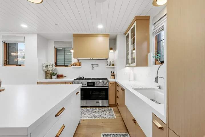Modern kitchen featuring white shaker island cabinetry, wood-finish lower and upper cabinetry, white countertops, wood-finish flooring, and a paneled ceiling