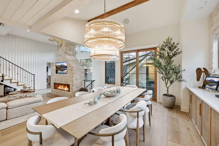 Spacious dining area featuring a tiered chandelier, wood-finish flooring, and a stone fireplace