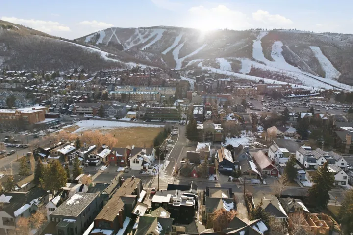 Snow-covered mountain backdrop, residential neighborhood with varied architectural styles, visible roadways, surrounding urban development, and open land areas