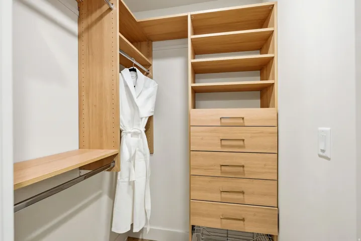 Built-in closet system featuring wood-finish shelving, multiple hanging rods, and a five-drawer dresser with metal pull hardware