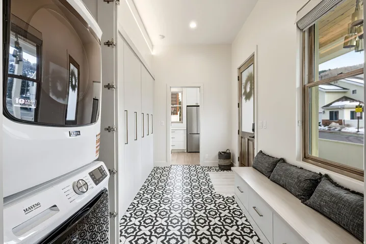 Stackable washer and dryer, patterned floor tile, built-in storage bench, wood-frame window, and recessed lighting